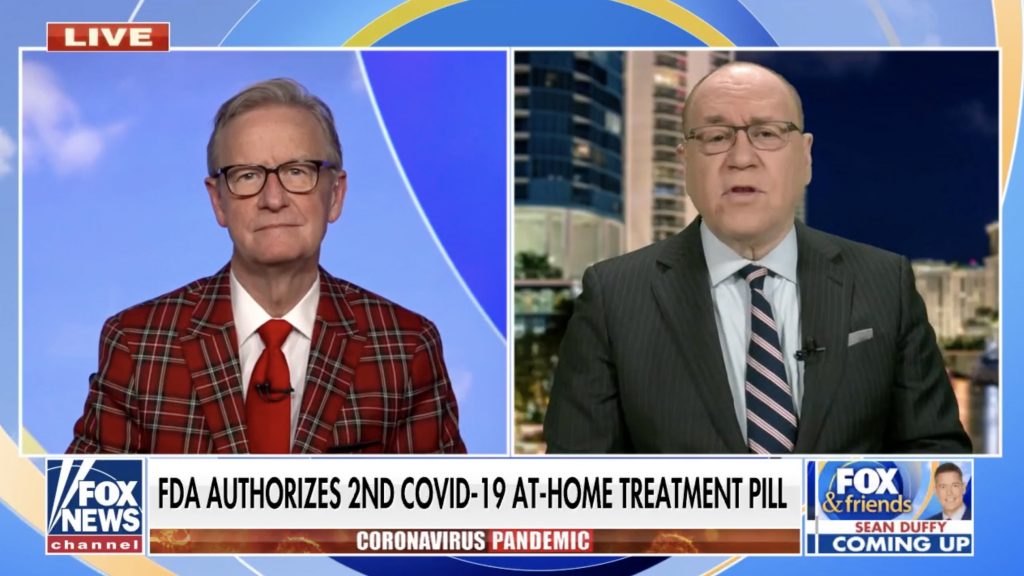 A split-screen television broadcast featuring two male presenters discussing a news segment. The left presenter is wearing a red plaid suit, and the right presenter is dressed in a formal suit and tie. The screen displays a headline about the FDA authorizing a second at-home COVID-19 treatment pill, with branding for Fox News Channel and Fox & Friends at the bottom.